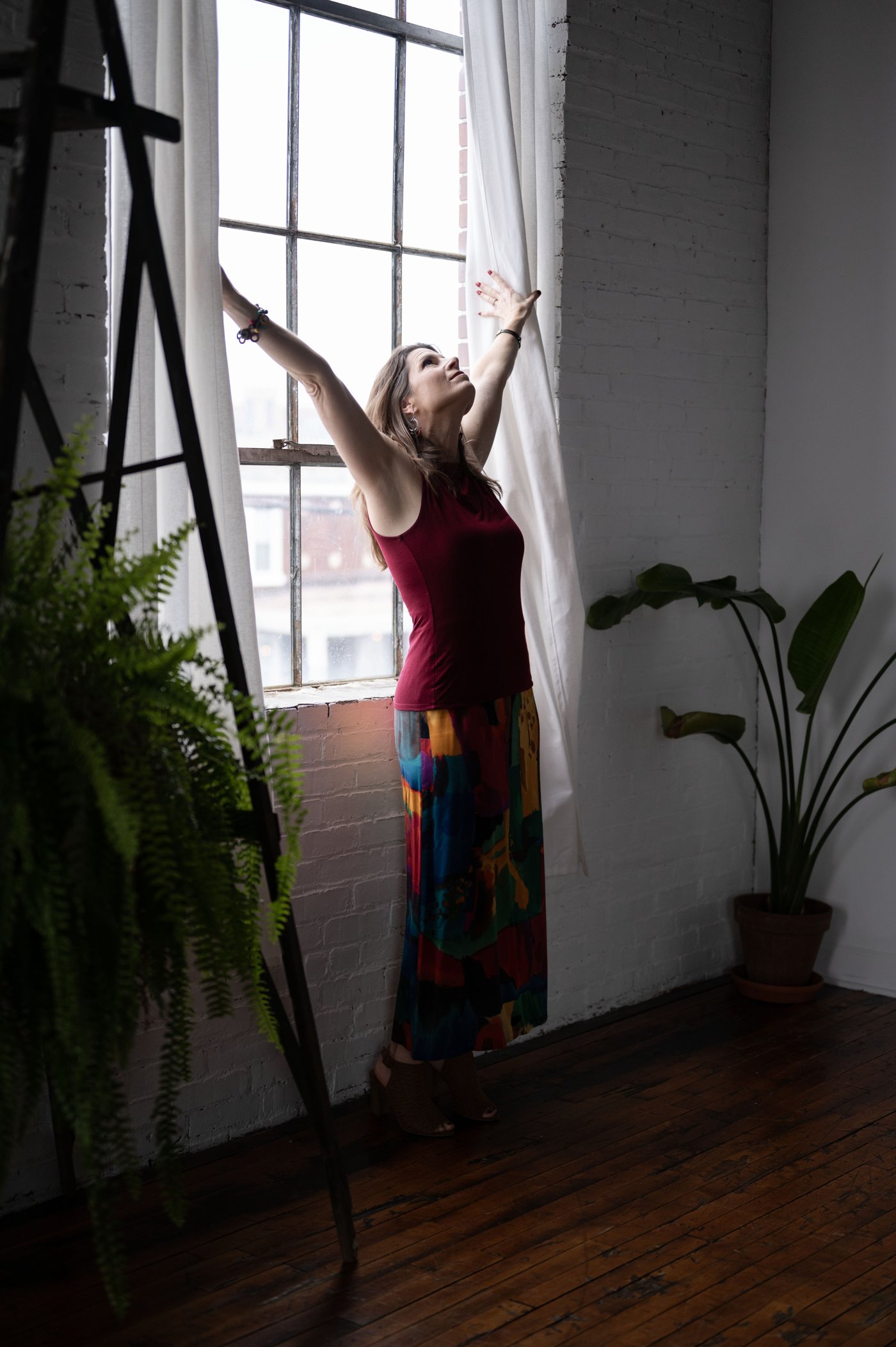 Woman reaching toward a sunlit window, arms raised in a moment of freedom and release